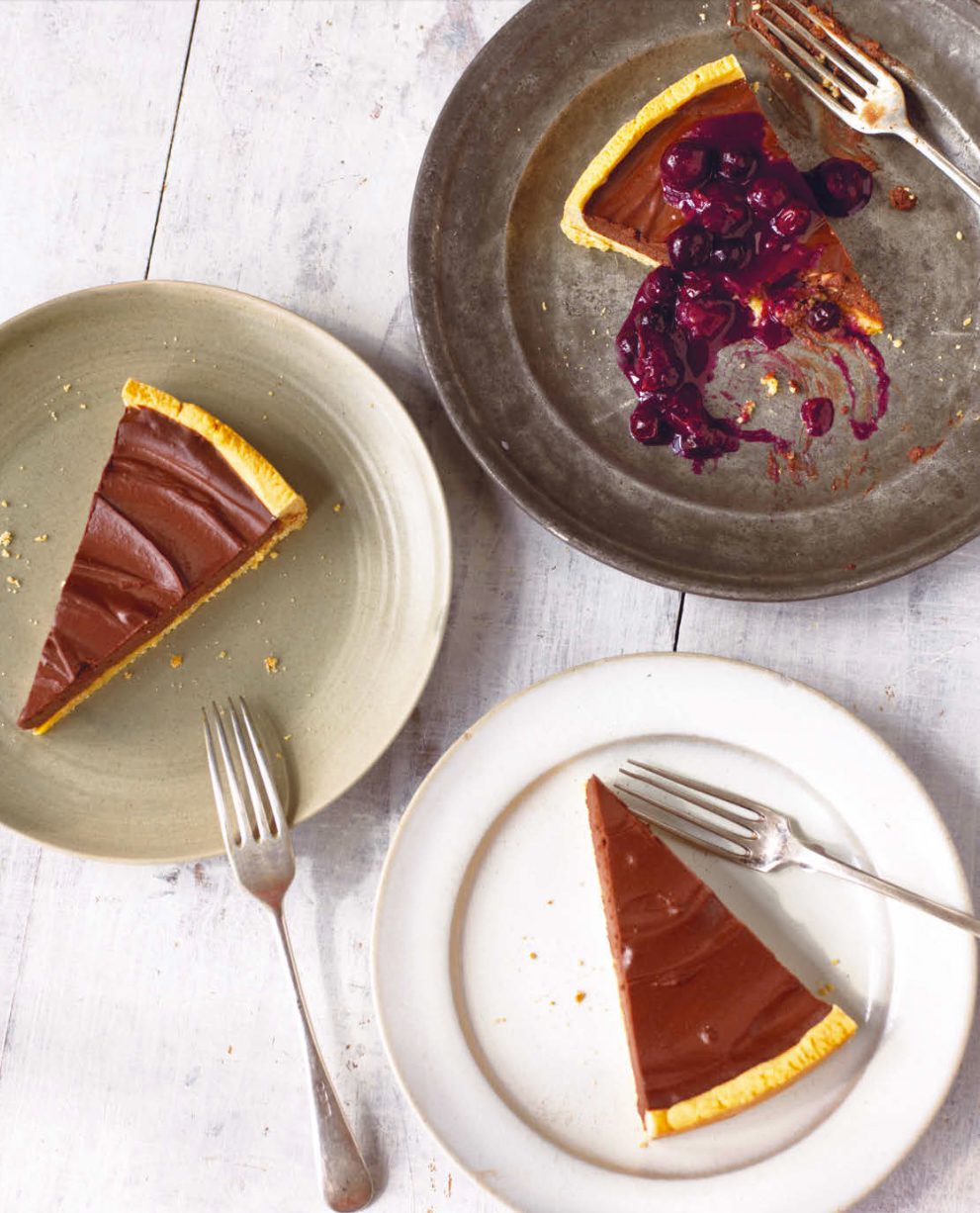 Slices of dark chocolate tart on plates, one topped with berry sauce.