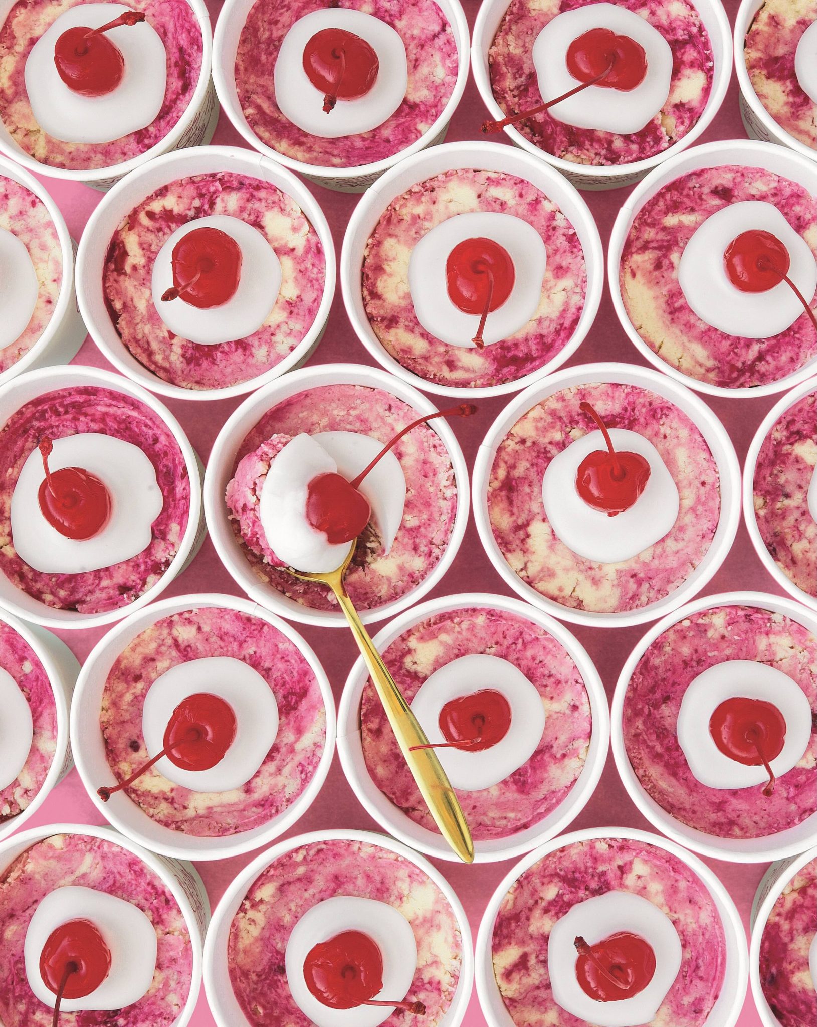 No-bake cookie dough cups with pink swirls, almond glaze, and cherries on top. 