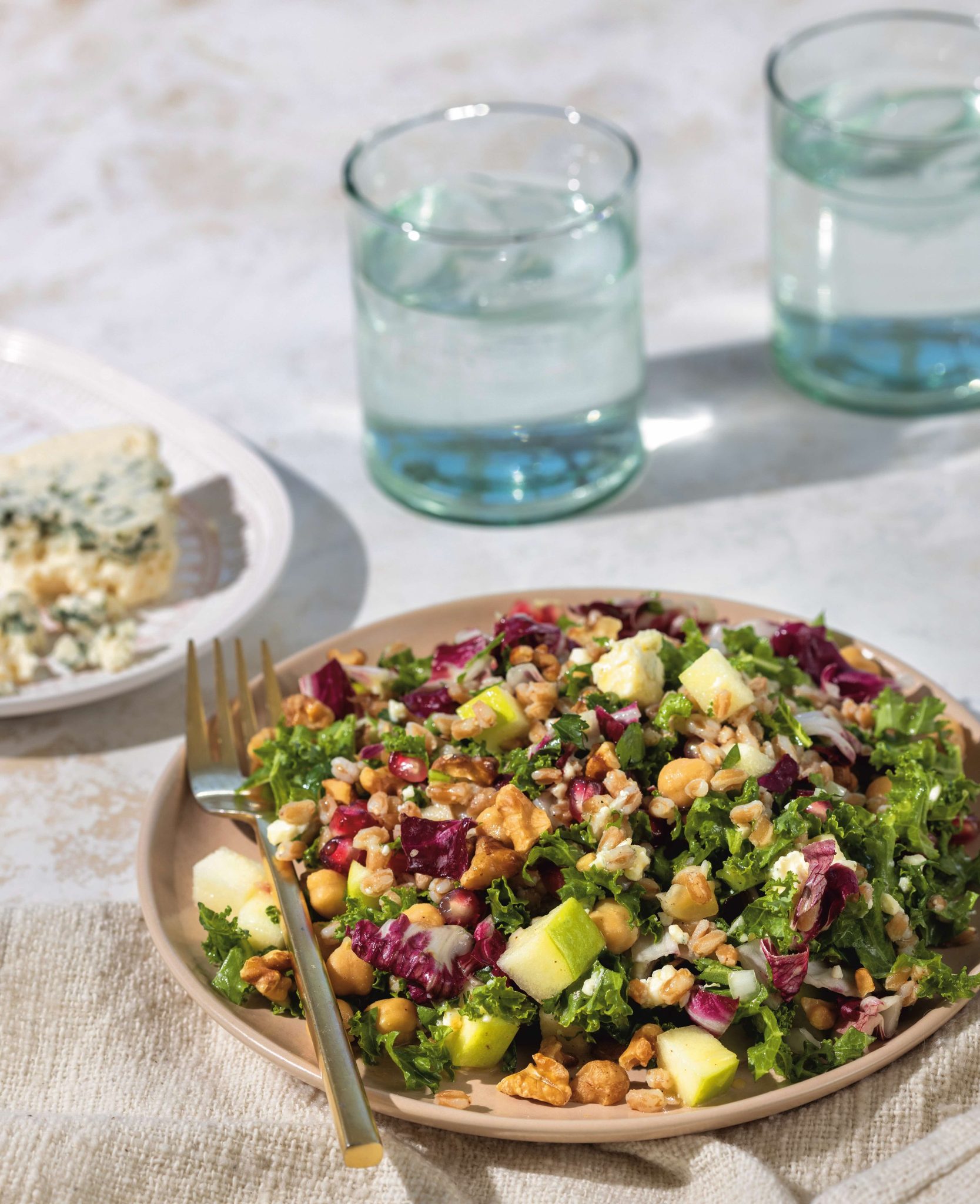 Farro salad with kale, apple, chickpeas, walnuts, and blue cheese on a beige plate.