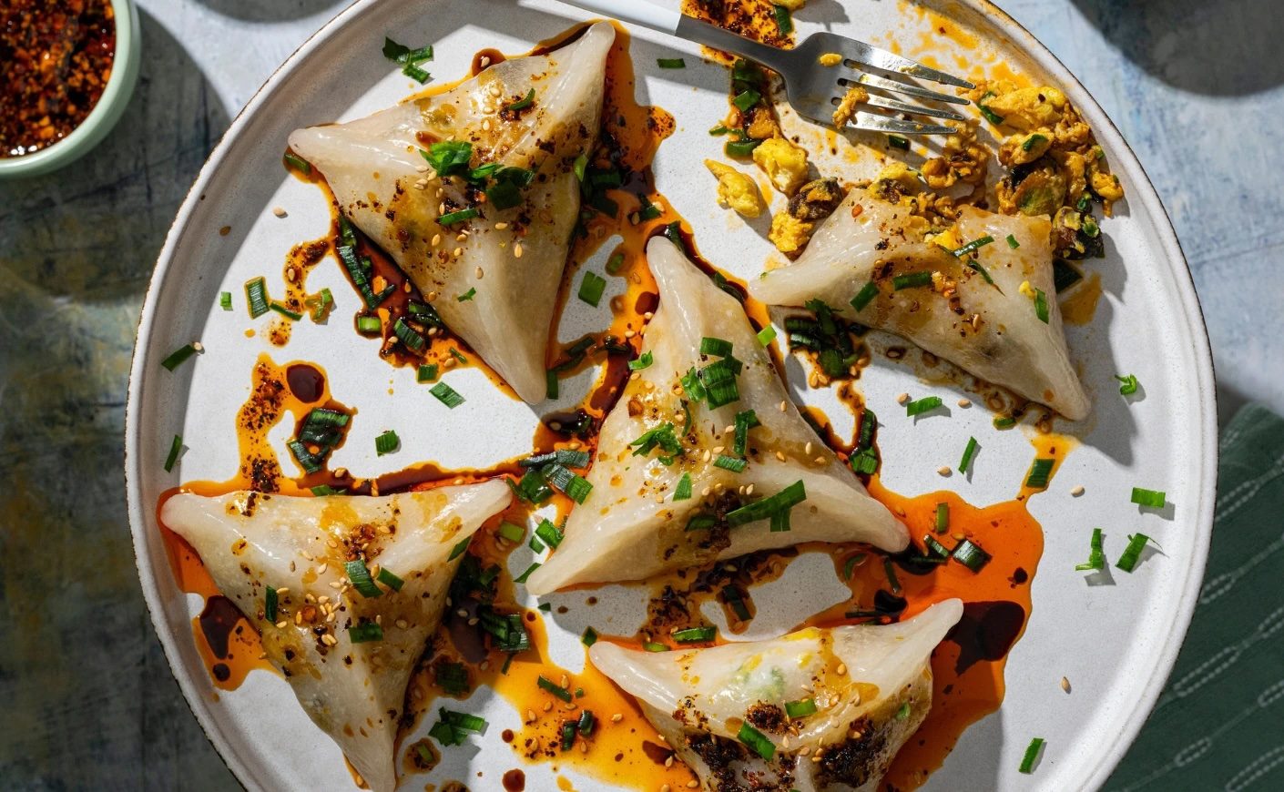 Plate of translucent Breakfast Crystal Bao with egg, chive, bacon, chili oil, scallions, and sesame 