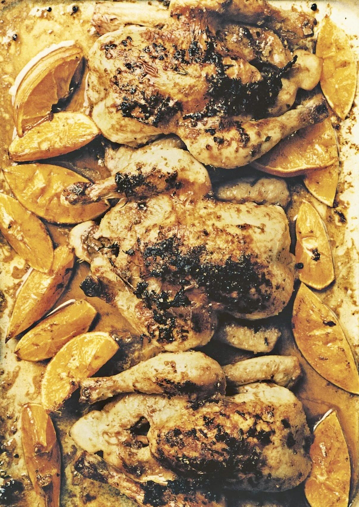 Golden-brown roasted Cornish hens with orange wedges, coated in a thyme and oregano marinade,