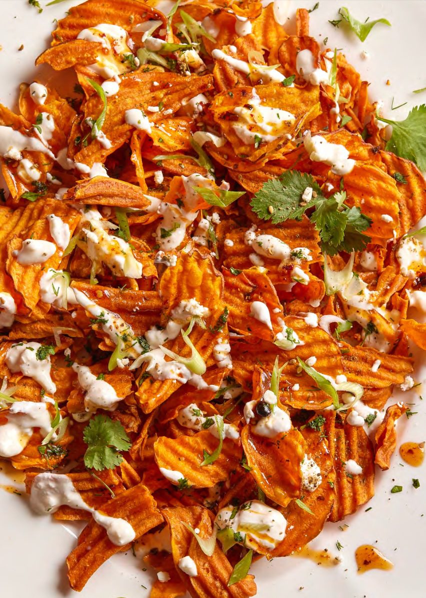 A vibrant plate of crispy sweet potato chips drizzled with creamy dressing.