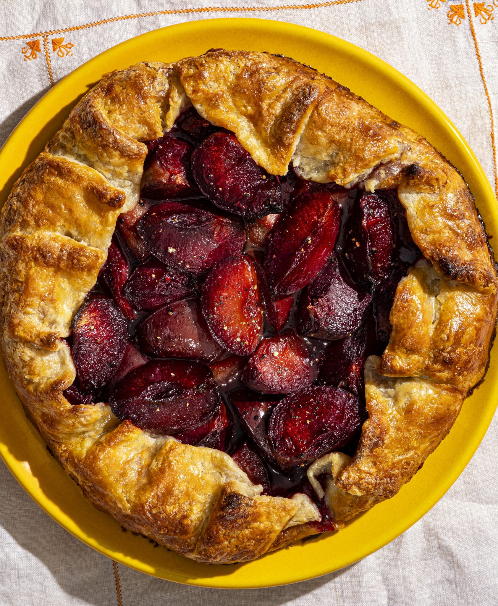Plum galette with golden crust and roasted sugared and peppered plums on a yellow plate.