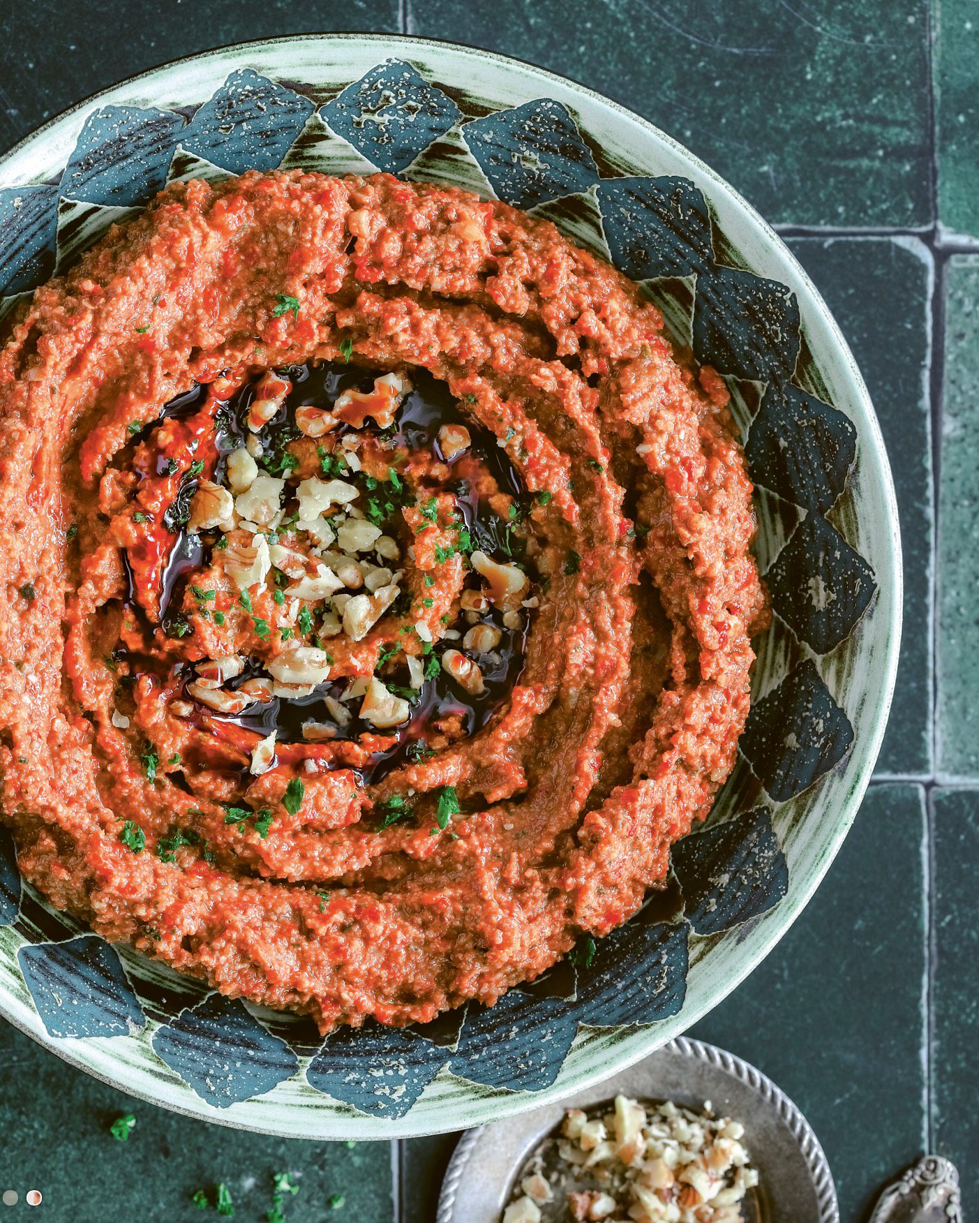 Red pepper and walnut dip topped with molasses, walnuts, and herbs in a patterned bowl.