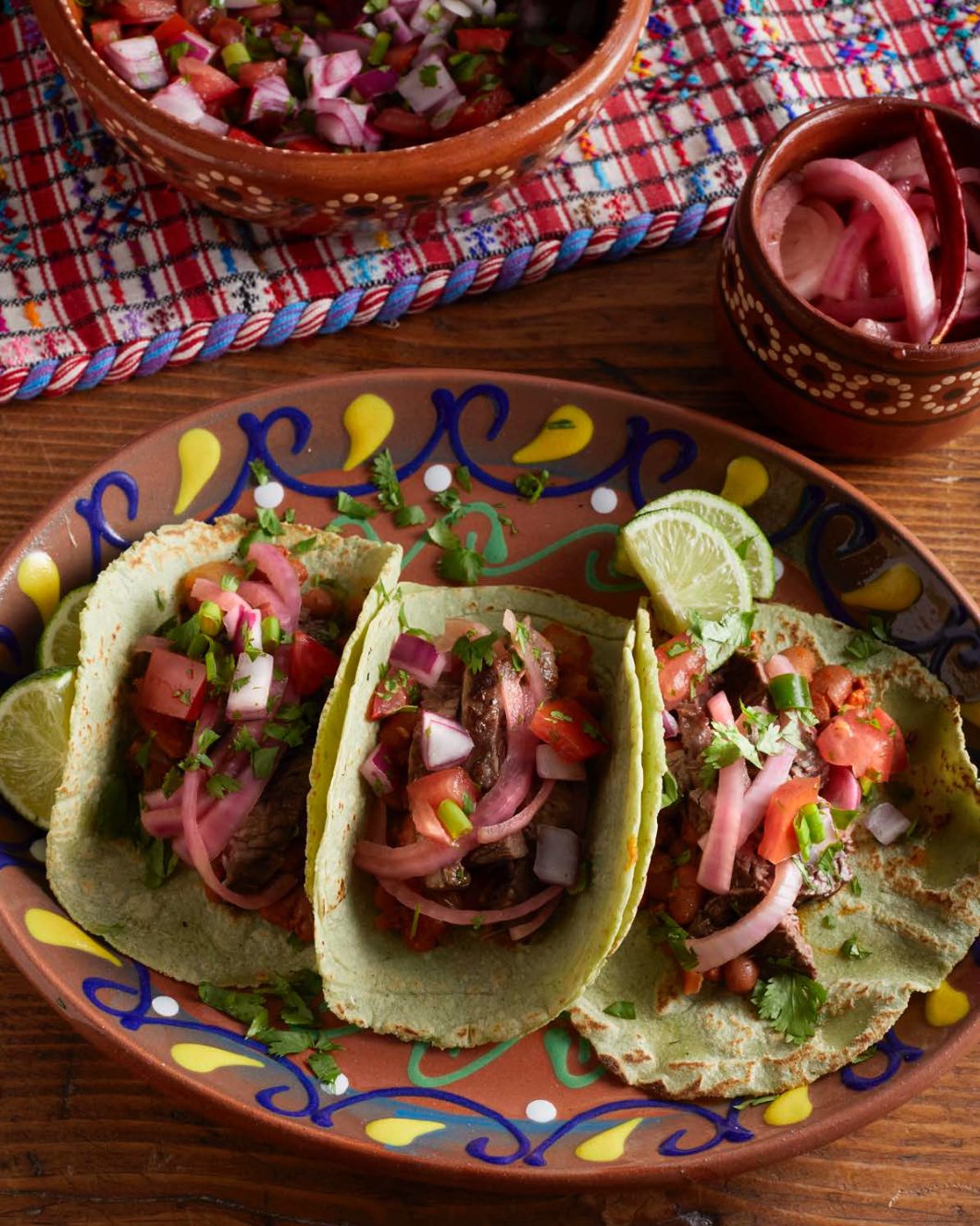 Grilled steak tacos with chorizo beans, pico de gallo, and pickled onions, served with lime wedges.