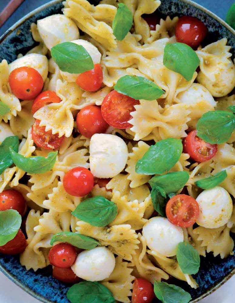 Bowl of farfalle pasta salad with cherry tomatoes, mozzarella balls, basil, and pesto.